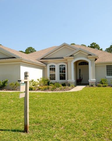 White Florida house with tall palms, green lawn, and a wraparound porch on a bright sunny day